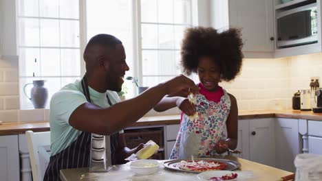 african american daughter and her father making pizza together in kitchen