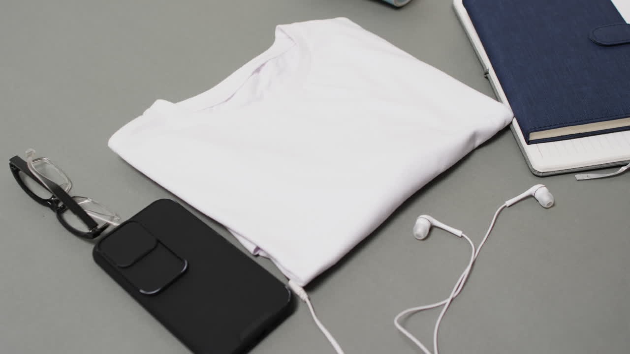 Video of white t shirt, smartphone and earphones with copy space on grey background