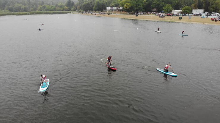 Chisinau, Moldova - October 10, 2021: Participants enjoy paddle boarding on a serene lake, surrounded by lush trees. The activity takes place under cloudy skies, creating a peaceful atmosphere