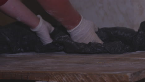 Raw-Dough-On-Wooden-Table-Covered-With-Black-Plastic