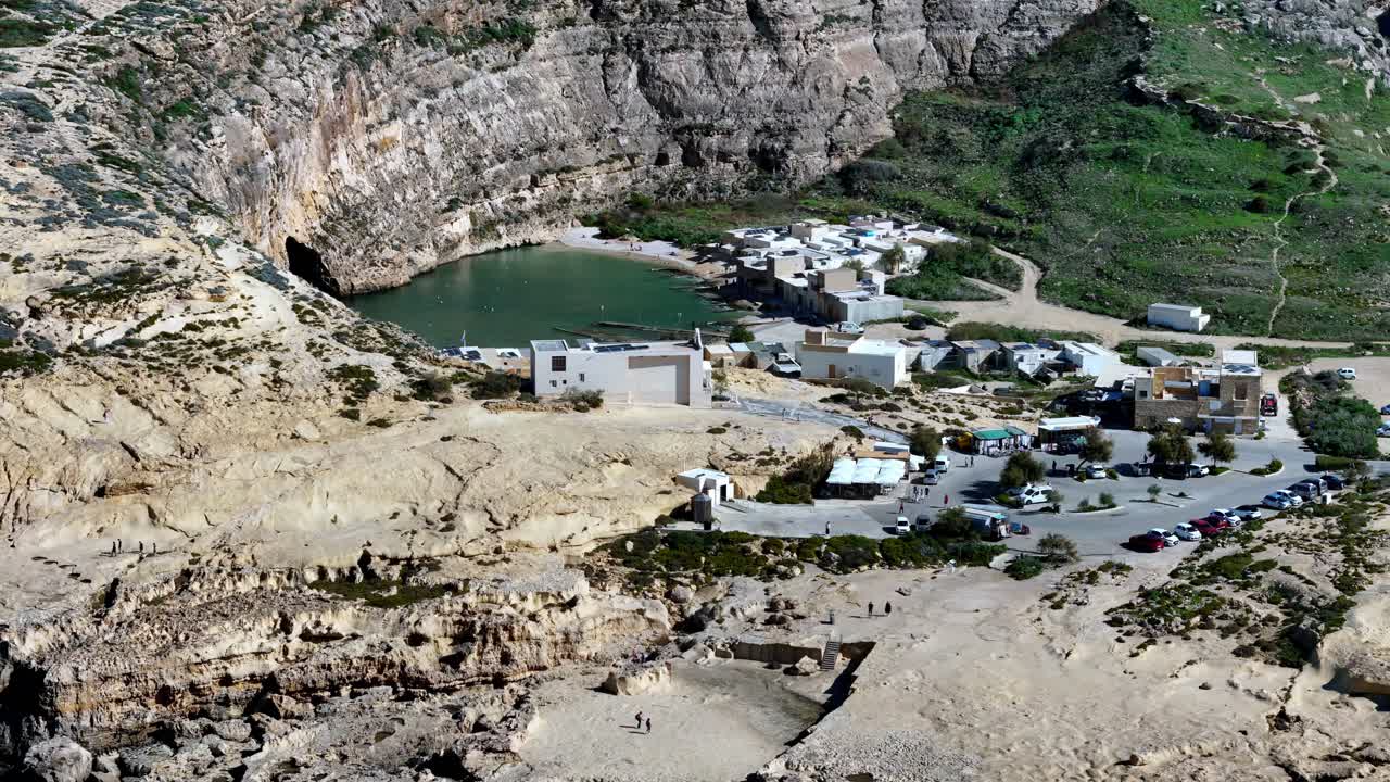 Toma amplia en picada del Mar Interior oculto en Dwejra, Gozo, durante un día de primavera soleado y brillante, con tranquilas aguas turquesas rodeadas de majestuosos acantilados de piedra caliza y rústicas viviendas costeras.