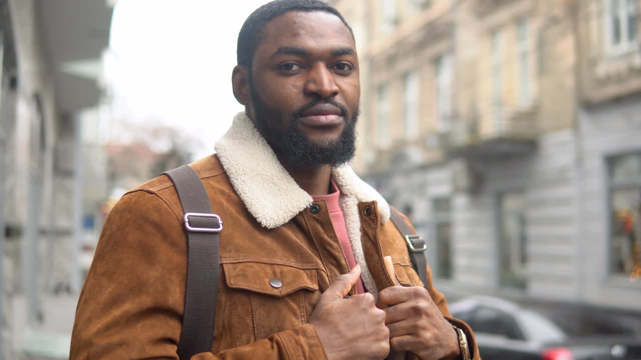 Bearded black with shoulder backpack stands outdoor near the office center