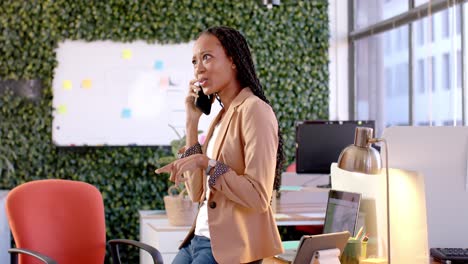 Happy-african-american-casual-businesswoman-talking-on-smartphone-in-office