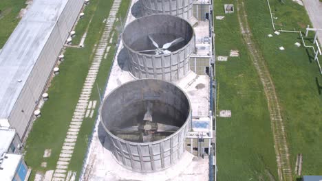 a top-down aerial shot pulls back to reveal a row of industrial cooling towers. the camera looks directly into the structures, showing the large fans and propellers spinning inside