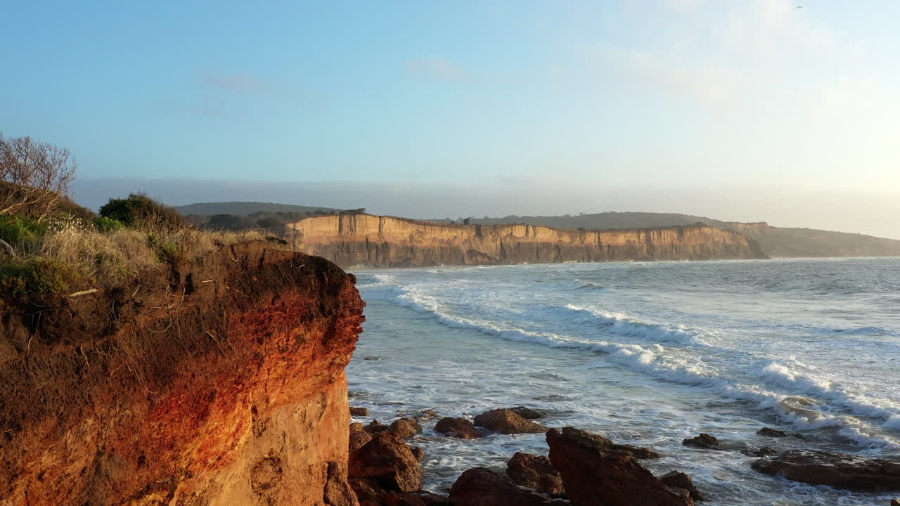 revelación aérea de olas rodando en acantilados erosionados durante la hora dorada