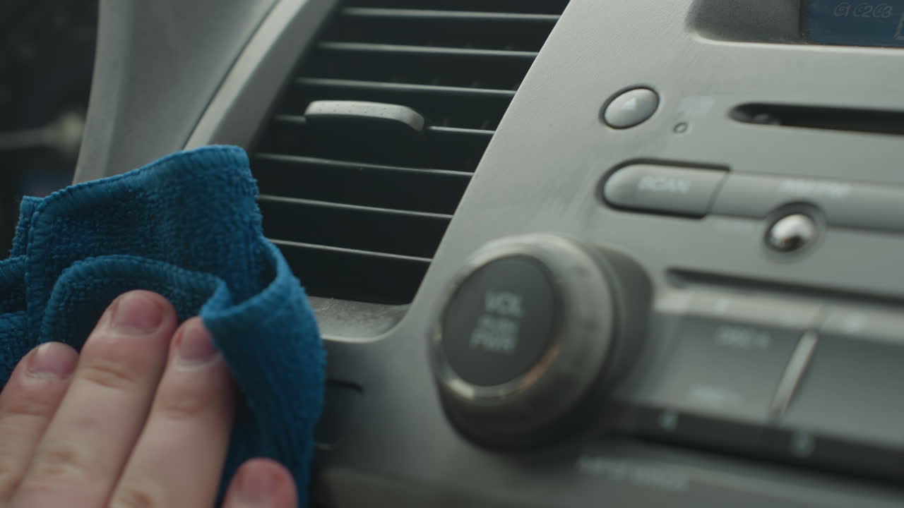 man cleaning dashboard inside car cabin with blue rag wiping console panel vent radio controls for interior detailing maintenance close up shot of hand motion care hygiene routine regular