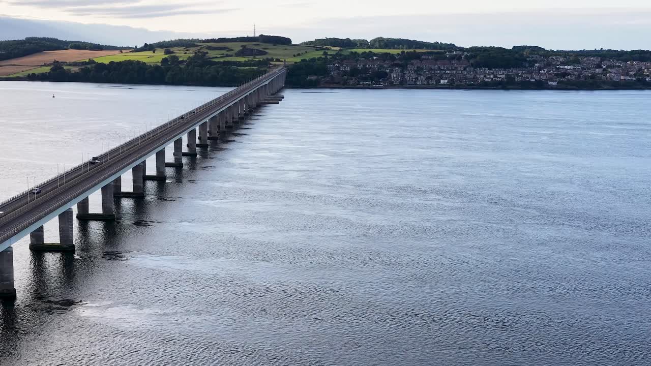 Drone glides toward Tay Road Bridge, revealing Dundee skyline, calm river, and soft daylight