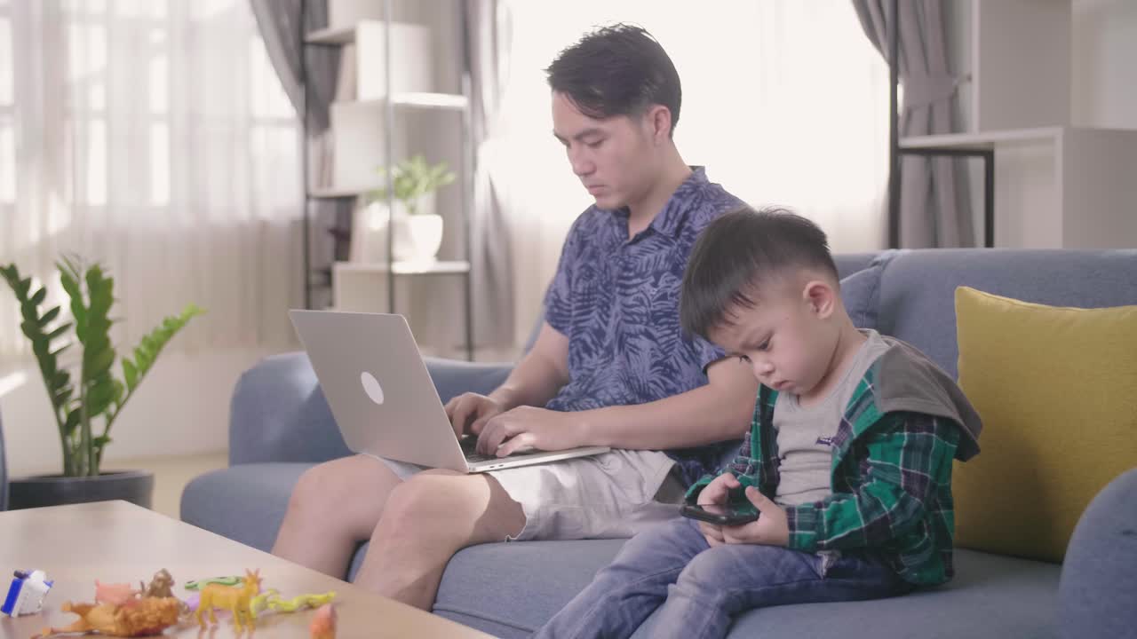 Boring Boy Using Smartphone While Father Working On Laptop