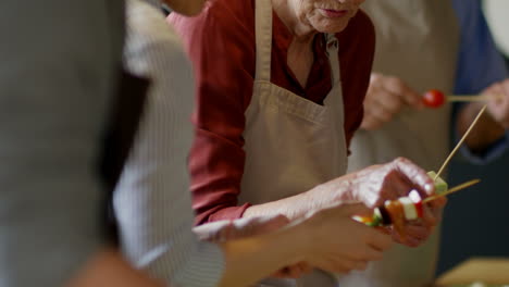 personas de diferentes generaciones paradas juntas en la mesa de la cocina y cocinando verduras shashlik