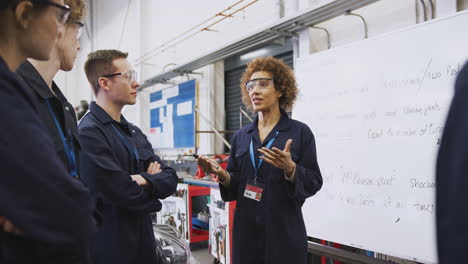 tutora femenina por pizarra con estudiantes que enseñan aprendizaje de mecánica automotriz en la universidad