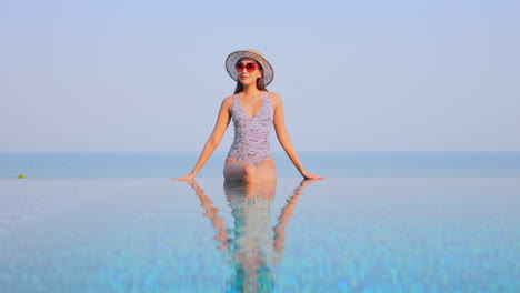 gorgeous asian woman sitting on infinity pool border leaning on hands and looking around slow motion static copy space template
