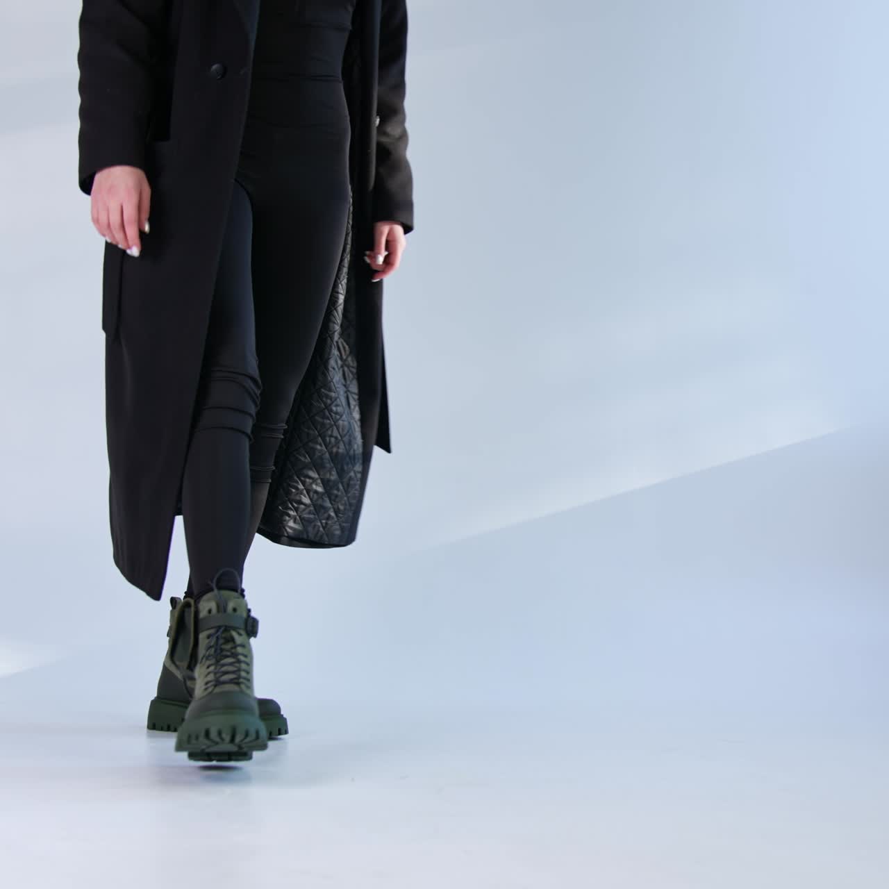 Unknown woman wearing black coat and jeans demonstrates army boots with little bag on the sides. Studio footwear presentation
