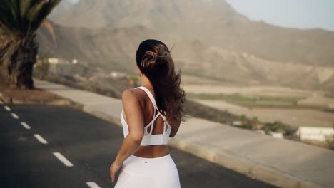 road runner woman running by asphalt road , jogging along the palm grove in white sport clothes