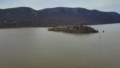 drone-footage-approaching-an-abandoned-castle-on-an-abandoned-island-in-the-middle-of-a-river-with-a-mountain-range-in-the-background