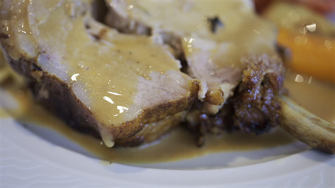 Close up of a portion of egg noodle near a few pieces of pork, cooked carrot and stuffed tomato on a white plate