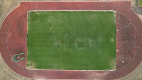 an aerial slowly zooming in of a weathered track and field or athletics field with a dusty exterior