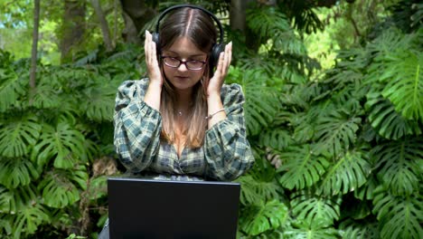 a young woman adjusting headphones while working online on a laptop in the park on a sunny day