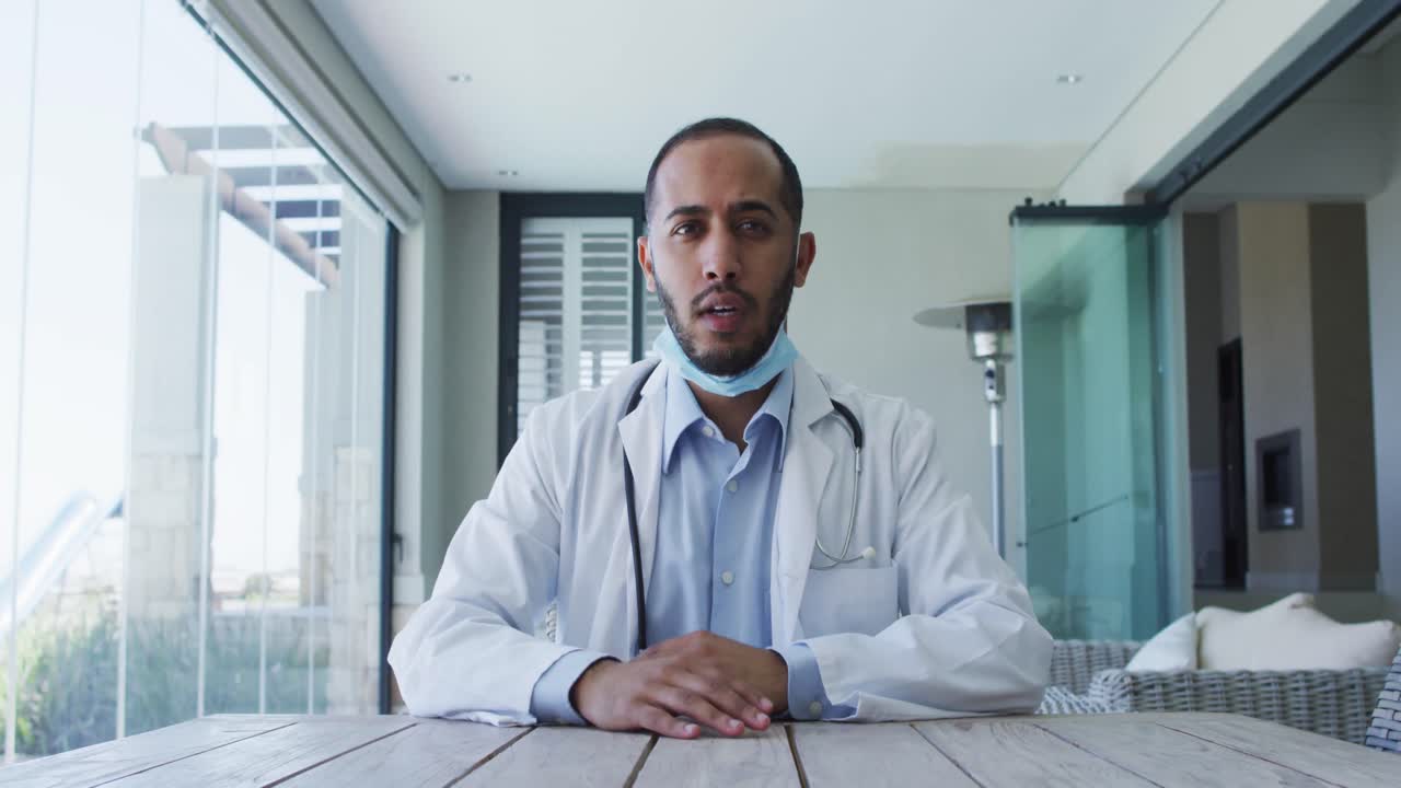 Medico uomo di etnia mista che indossa una mascherina e parla durante una videochiamata.
