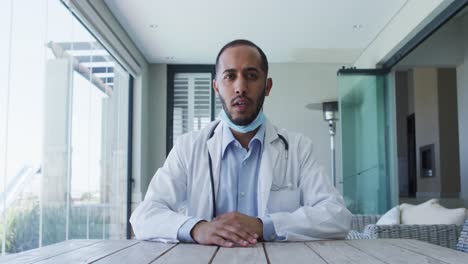 Mixed-race-male-doctor-wearing-face-mask-talking-during-video-call