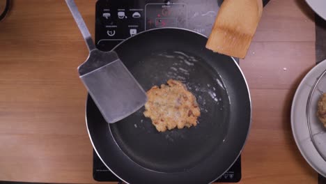 cooks hands turning over small fried vegetable pancake with spatula and ladle