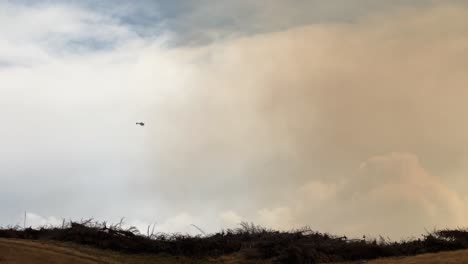 Helicopter-flying-towards-thick-brown-wildfire-smoke-in-Twizel,-New-Zealand-2023