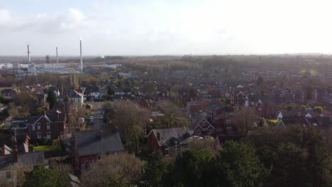 Aerial-view-over-park-trees-to-industrial-countryside-townscape-neighbourhood-in-Merseyside,-England