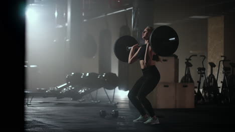 female bodybuilder doing exercise with weights in gym. a female weightlifter performs a barbell lift in a dark gym. female bodybuilder does weight lift workout exercises in the hardcore training