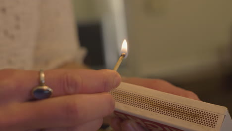 close-up-of-a-woman's-hand-striking-a-wooden-match-holding-it-as-it-burns