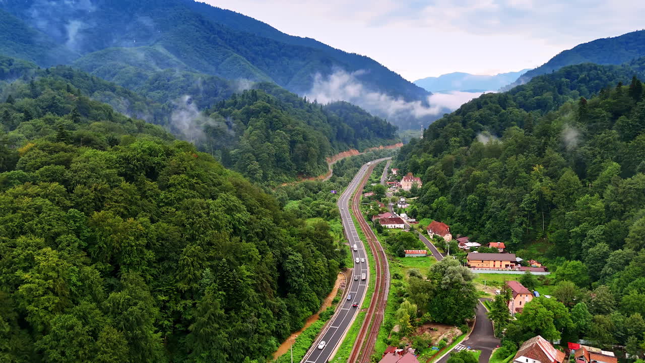 Romanian Carpathians with road and village. A winding road and railway pass through a forested valley village in the Carpathian Mountains of Romania