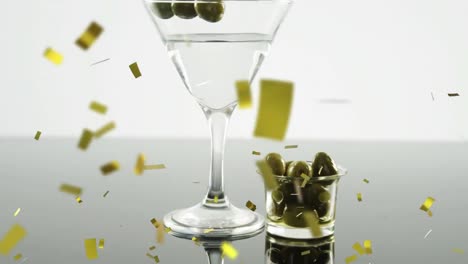 Golden-confetti-falling-over-cocktail-glass-and-olives-against-grey-background