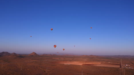 Colorful-hot-air-balloons-flying-over-mountains-and-desert-landscape-during-sunrise