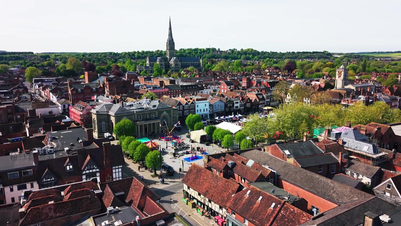 Drohnenaufnahmen aus der Luft vom Stadtzentrum von Salisbury mit der Kathedrale von Salisbury im Hintergrund, die Dächer, historische Straßen, die Guildhall, den Marktplatz, Bäume und Verkehr zeigen