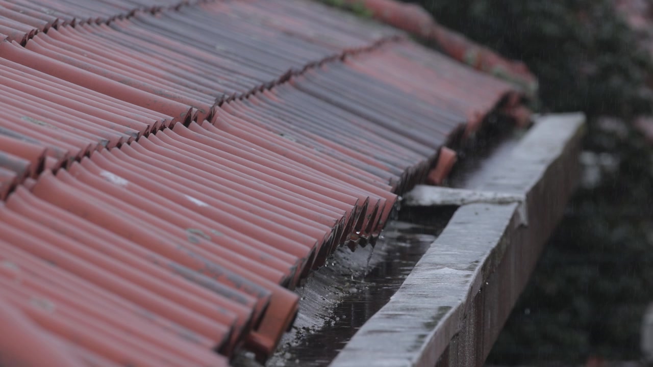 Rain pouring on roof tiles onto roof gutter system. Rain water collection.