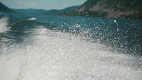 water roars and foams on lake while boat moves. majestic landscape of water massif on summer day. shiny white splashes rises high into air above body of water slow motion