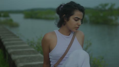 Middle-shot-of-a-stylish-young-Indian-woman-in-a-purple-dress-stands-by-the-tranquil-river