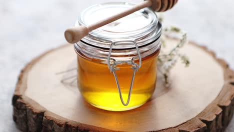 glass jar full of fresh honey placed on slice of wood