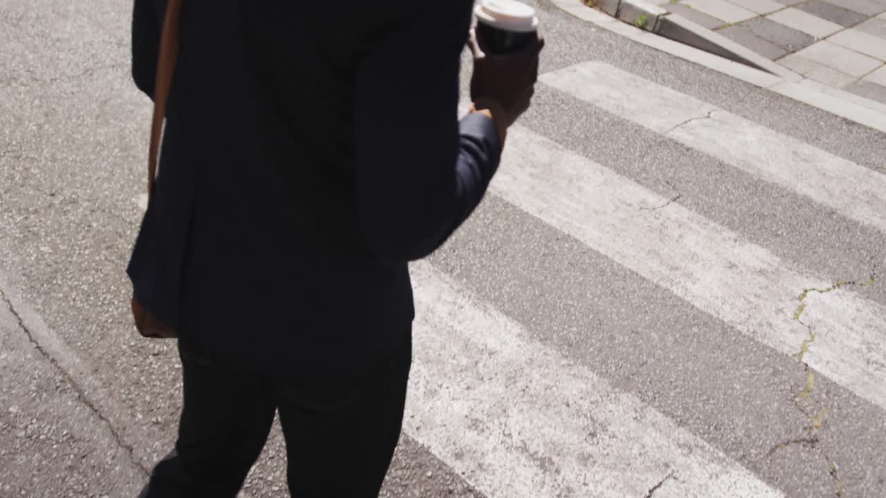 Low section of african american businessman carrying takeaway coffee walking on zebra crossing
