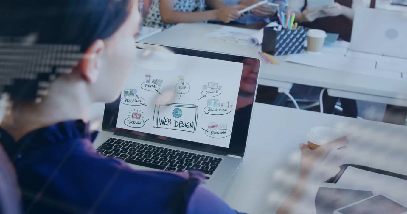 Pointing colleague woman holding coffee typing on laptop at open-plan office working on web design