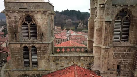 drone-shot-revealing-Saint-Bonnet-le-Chateau-collegiate-church-and-village-in-Monts-du-Forez-on-an-overcast-day,-Loire-departement,-France