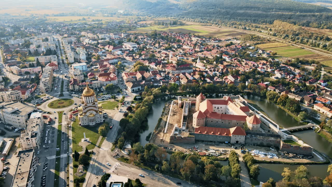 Luftdronebilde av Făgăraș i Romania. Johannes Døperens kirke og Făgăraș Citadel, bygninger, veier med biler, grøntområder og åser