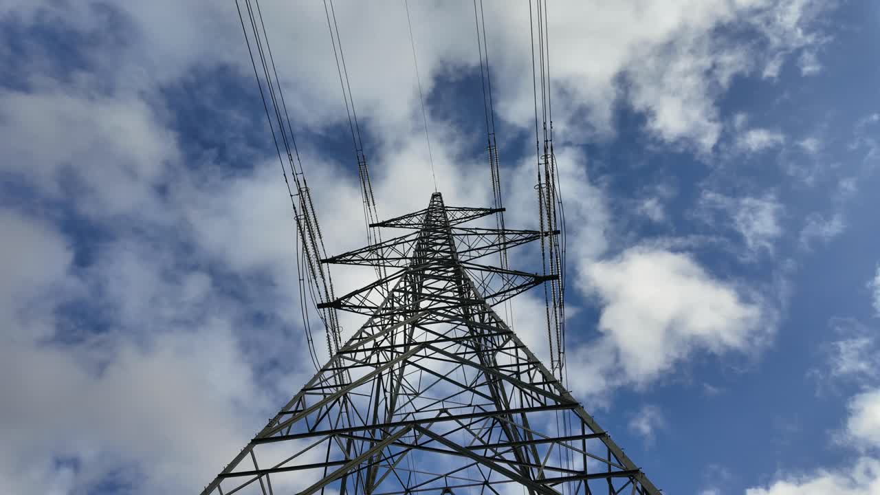 Time-lapse looking up at a high voltage transmission tower with fast moving clouds