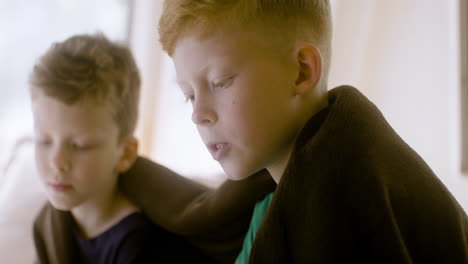 two little brothers with blanket on their shoulders sitting on bed in a campervan and reading a book