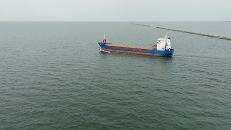 aerial establishing view of large blue cargo ship leaving port of liepaja , karosta bridge, slight overcast day, calm baltic sea, wide drone dolly shot moving left