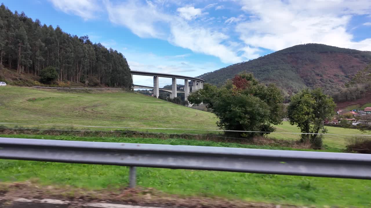 Large concrete highway bridge crosses open countryside under cloudy sky, filmed from distance in slow motion