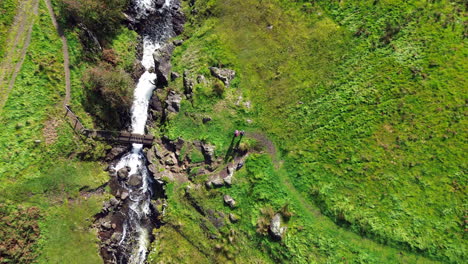 Rising-birds-eye-view-of-bridge-over-stream-and-couple-stood-nearby