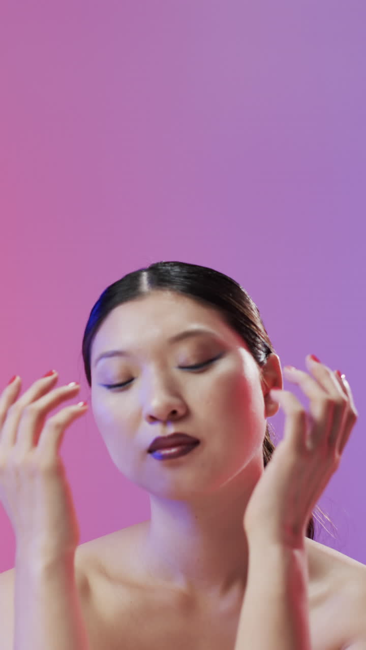 Vertical video of asian woman with black hair and make up looking at camera, copy space, slow motion