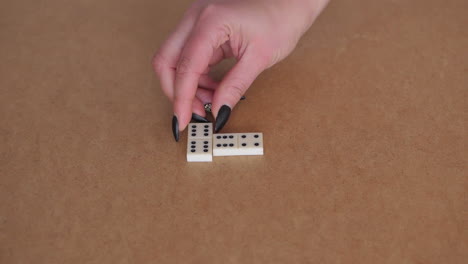 female hand placing white domino next to another one on table