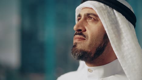 portrait of successful arab businessman in traditional outfit gently smiling, wearing white kandura and black agal keeping a ghutra in place. saudi, emirati, arab businessman concept.