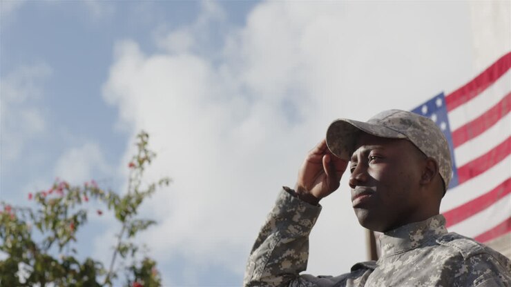 Saluting, soldier in uniform standing outdoors with American flag in background