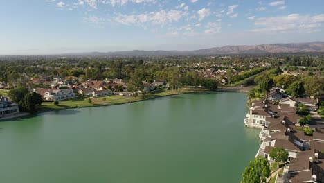 drone flying over woodbridge north lake over houses, with blue skies, green lake, and sunny 2022 summer day